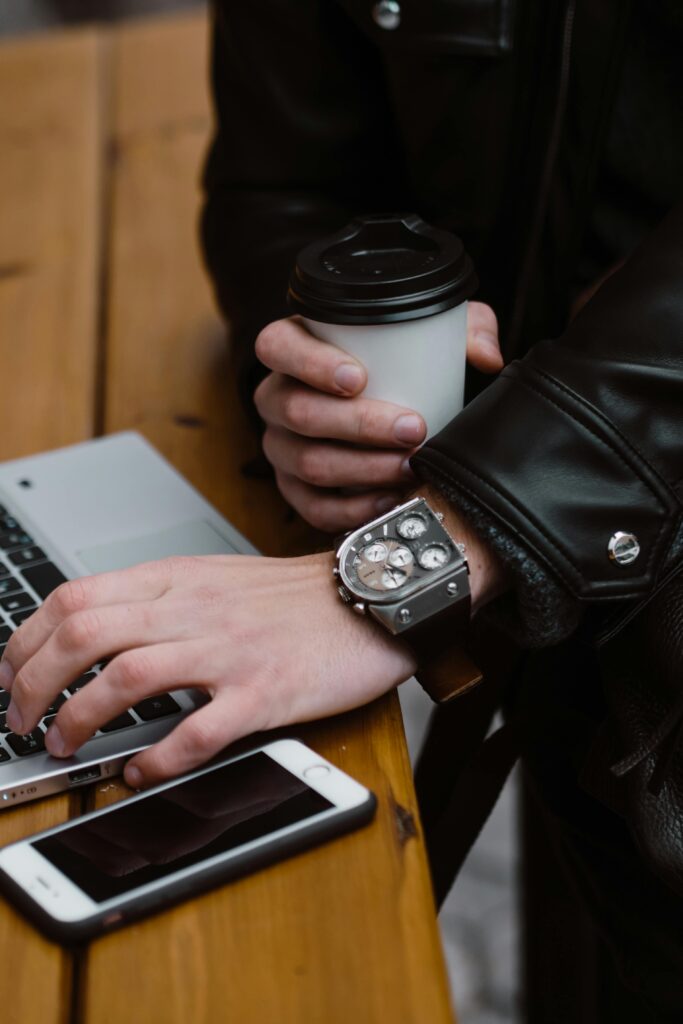Close-up of a person working on a laptop while holding a coffee cup, showcasing a wristwatch.